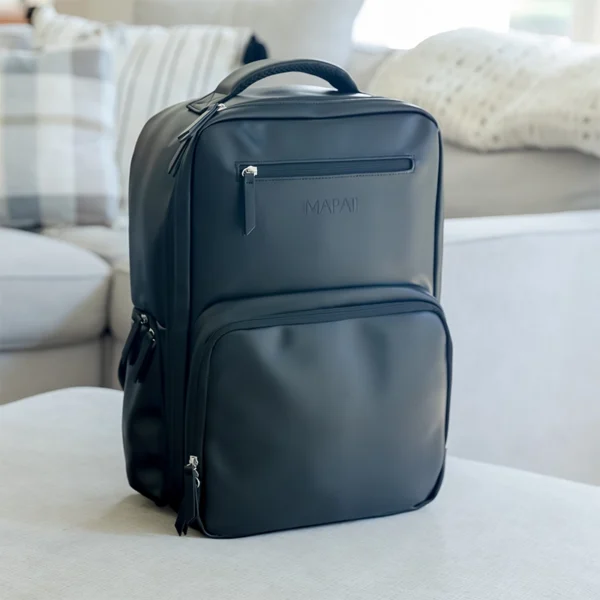 Black Mapaii diaper backpack displayed on a modern white couch in a bright living room.